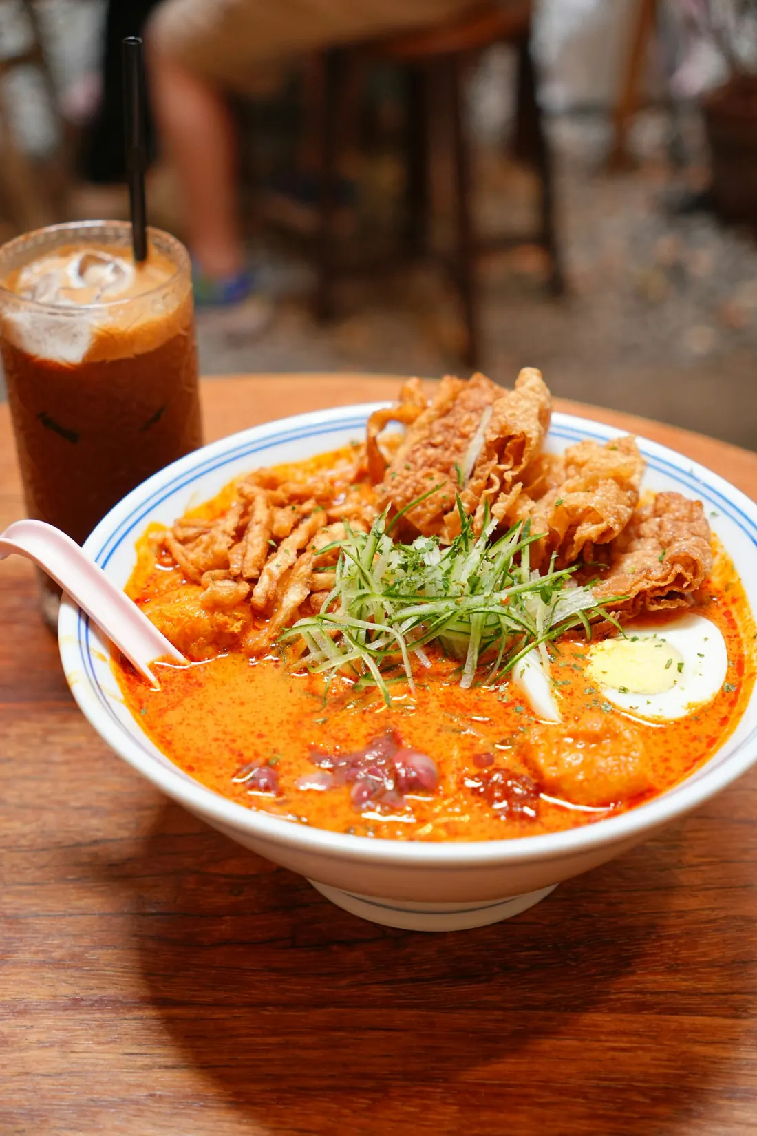 A bowl of laksa with an iced drink