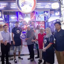 A group of staff and guests gathered in front of the lit shopfront in the evening
